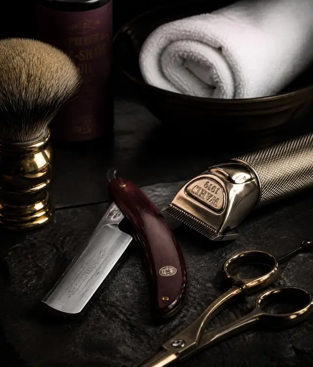 Straight razor, clippers, shears and a hot towel on dark slate